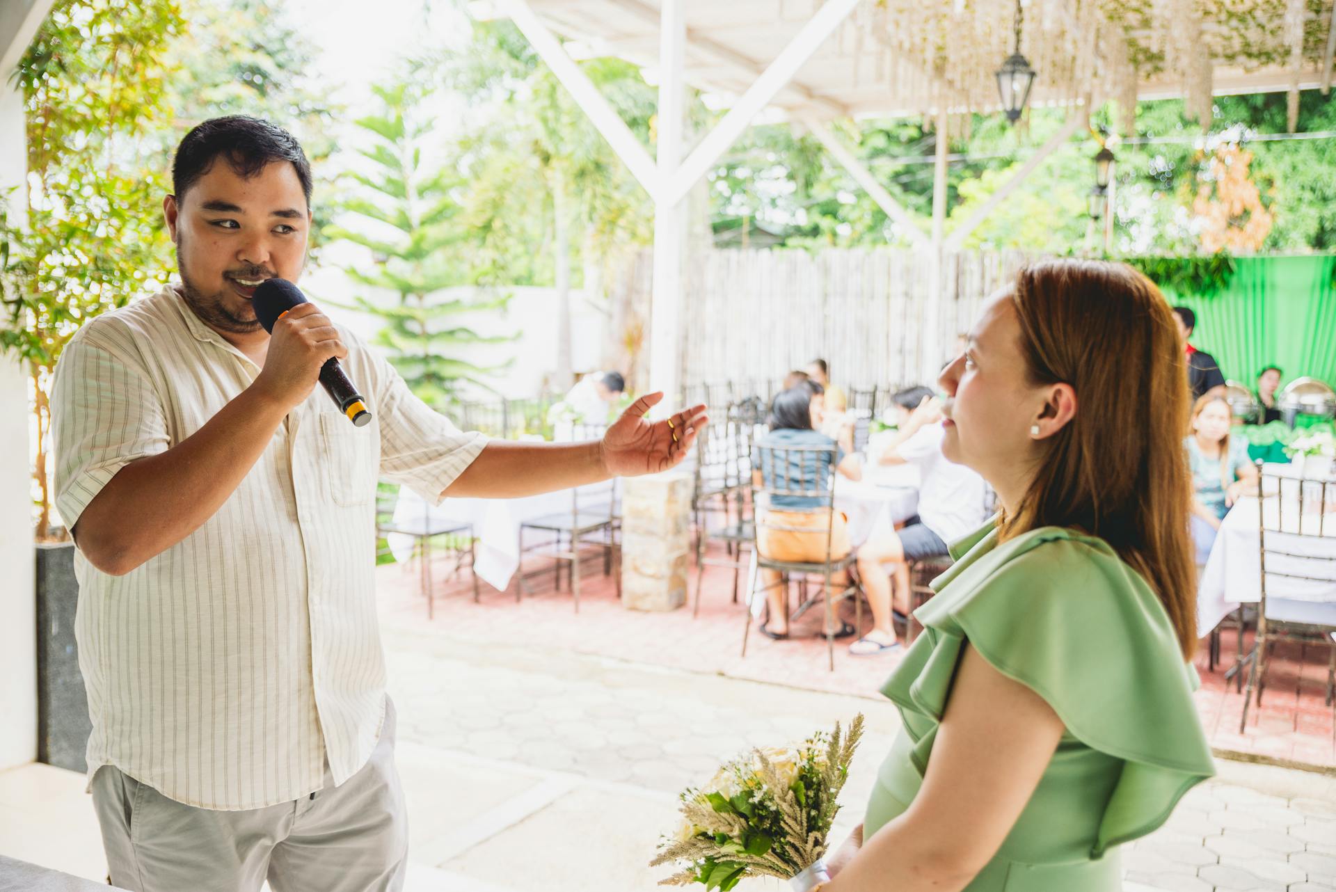 Besišypsantis renginių vedėjas su mikrofonu bendrauja su šventės dalyviais prabangiai papuoštoje salėje.