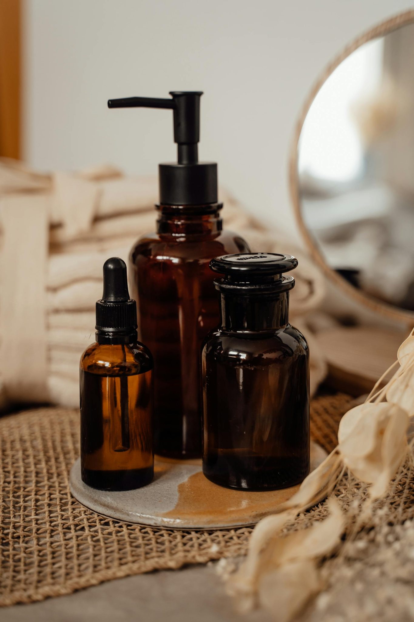 Estetiškai išdėstytos natūralios kosmetikos priemonės stikliniuose indeliuose ant šviesaus paviršiaus rytinėje šviesoje.